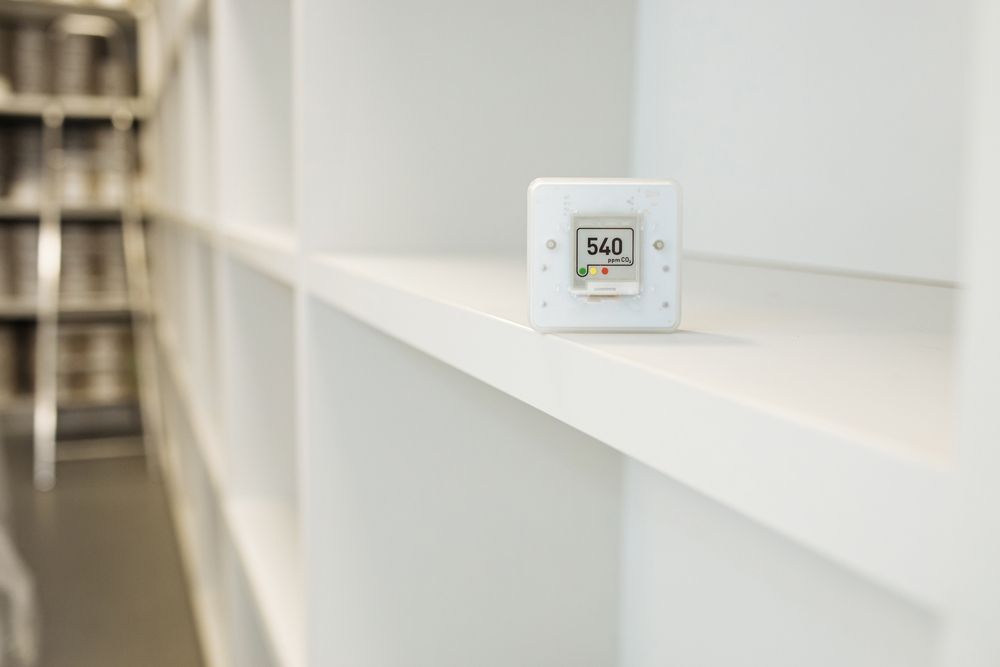A white thermostat is sitting on a white shelf in a library.