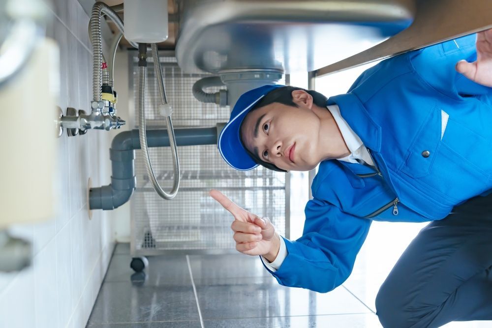 A man in a blue jacket and hat is pointing at a sink.