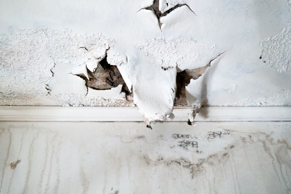 A white wall with peeling paint and a hole in it.