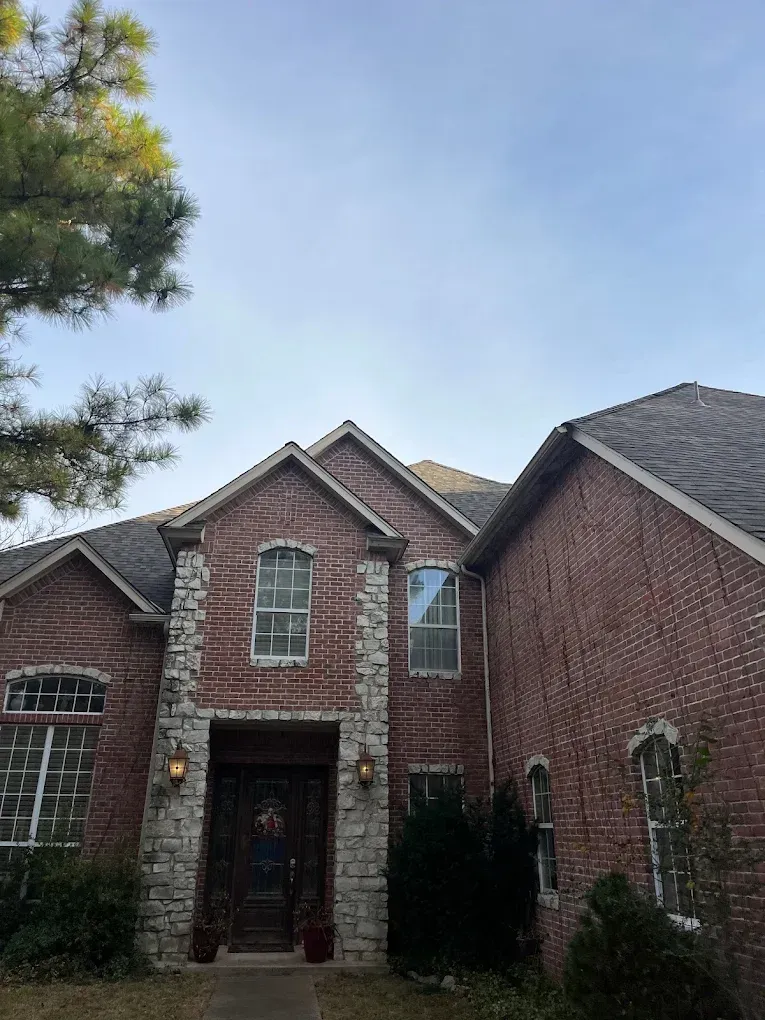 Two-story red brick house with stone accents, windows, and dark brown roof under a cloudy sky.