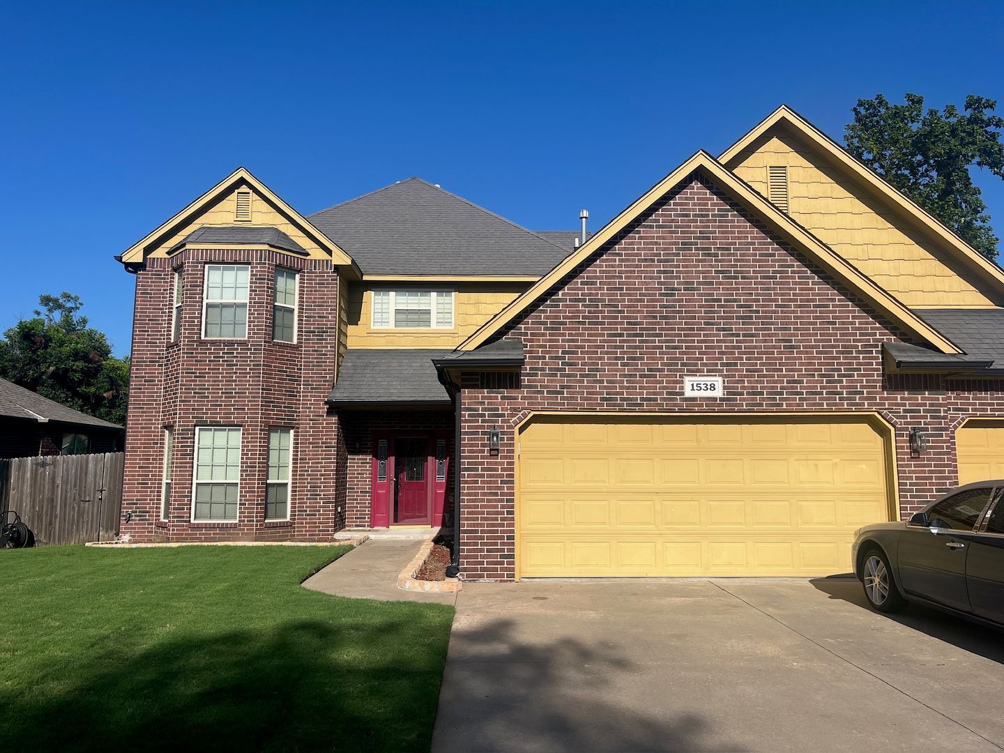 Two-story house with brick and yellow siding, a garage, and a car parked in the driveway on a sunny day.