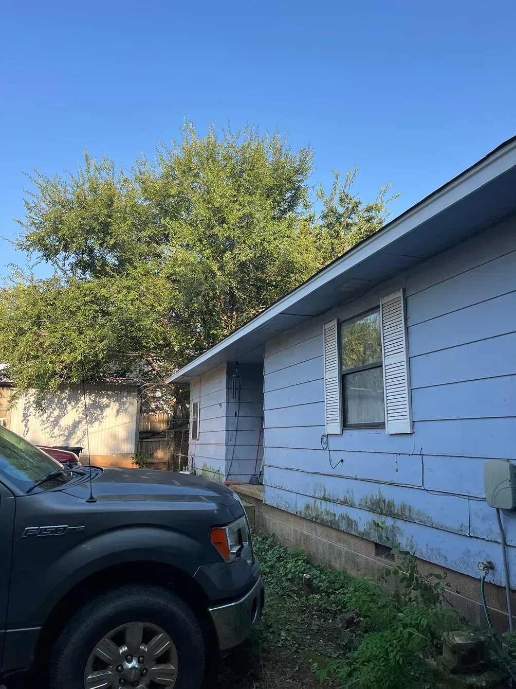 Blue house with white trim and a parked gray truck on a sunny day.
