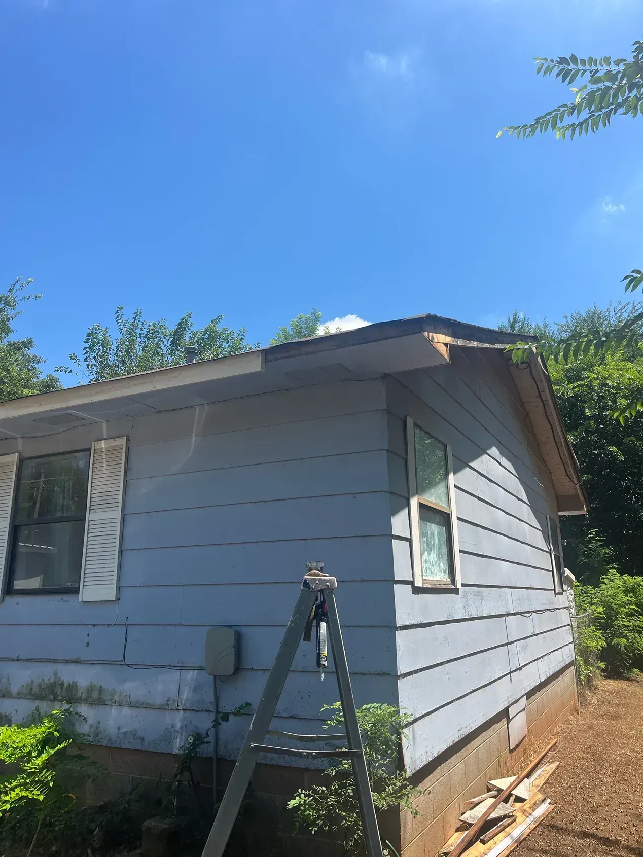 Blue house with roof repair underway; ladder and materials visible.