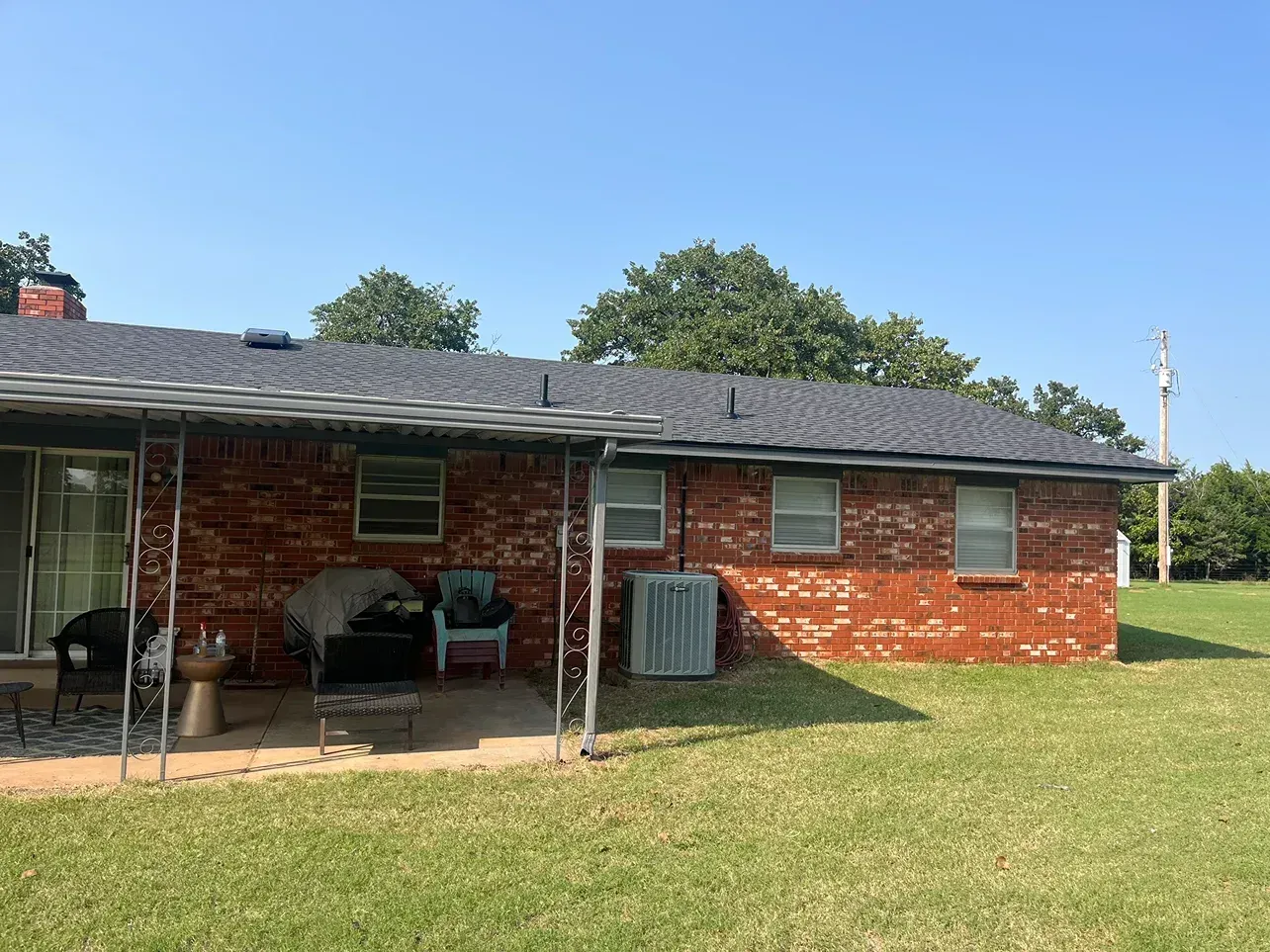 Brick house exterior with covered patio and green lawn on a sunny day.