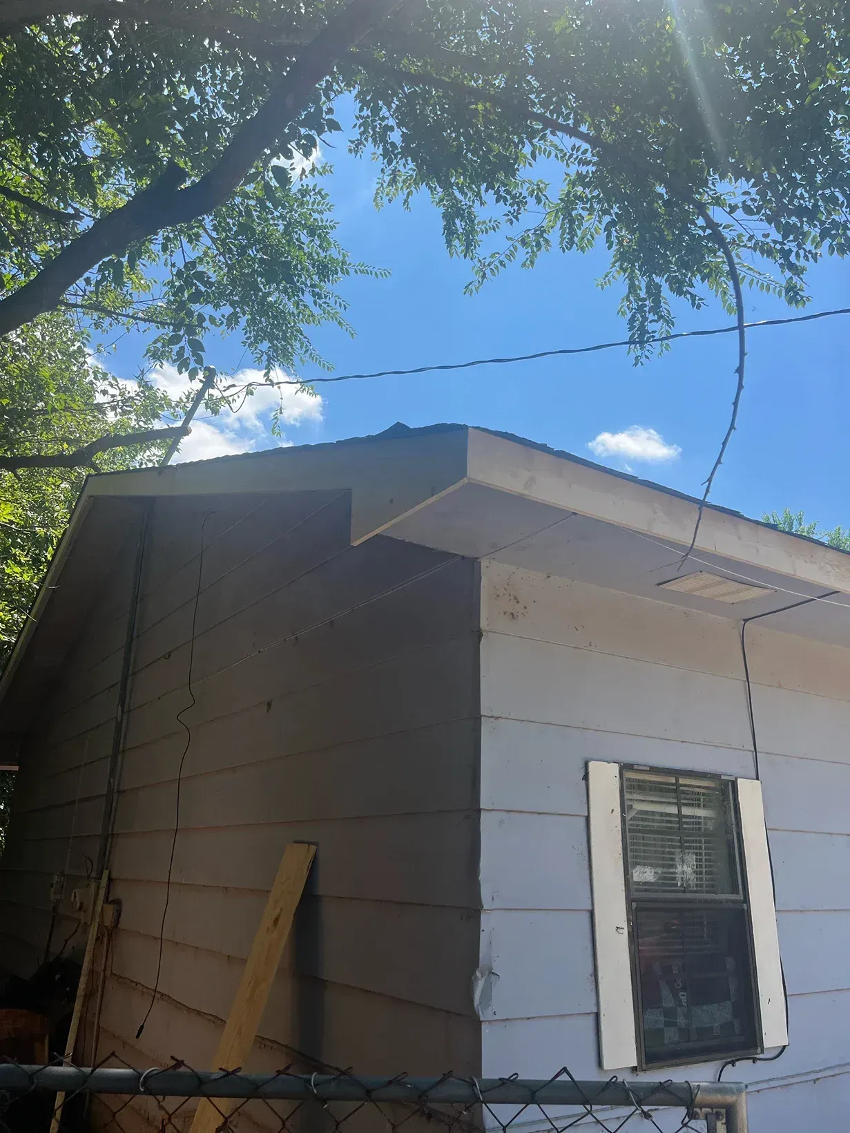 Side view of a white and gray building with a blue sky visible through the trees.