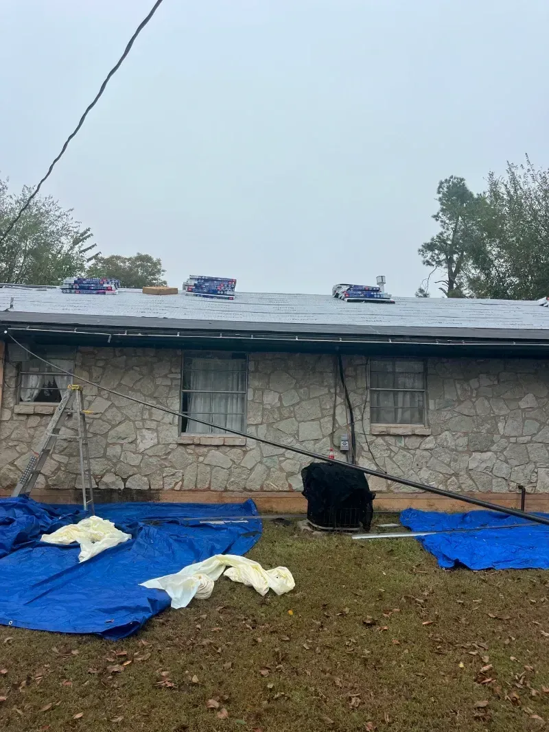 House with damaged roof covered by blue tarps.