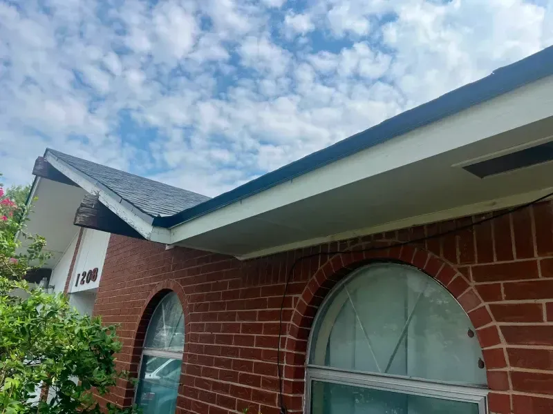 Brick house with dark roof and white trim against a cloudy sky.
