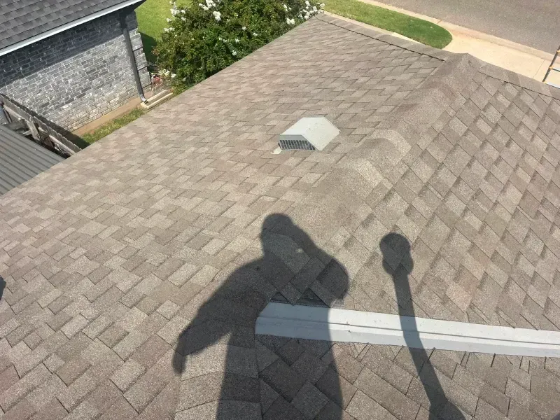 Overhead view of a roof with brown shingles, a skylight, and a person's shadow.