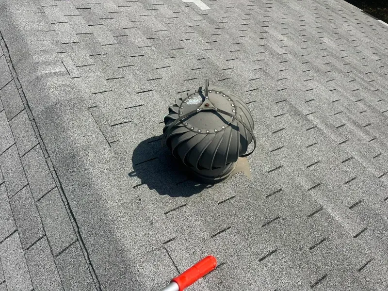 Turbine roof vent on a gray shingle roof, with a red-handled tool visible in the foreground.