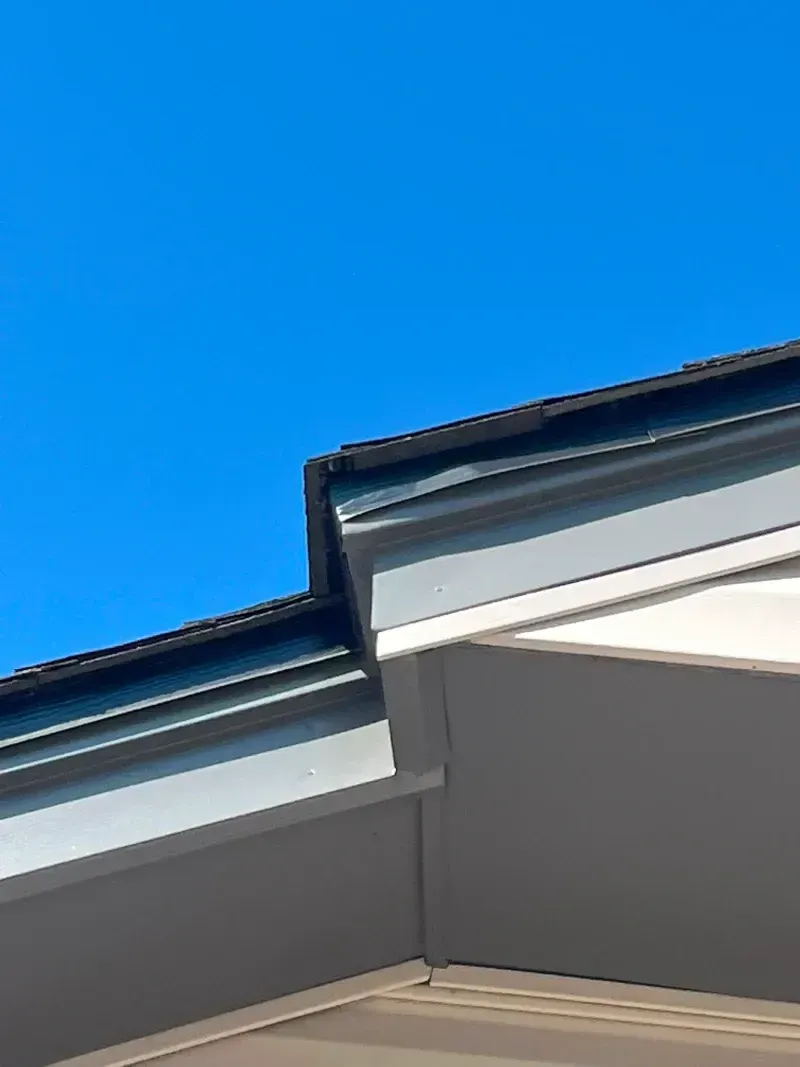 Blue sky with a section of a roof's edge; black, gray, and white layers.