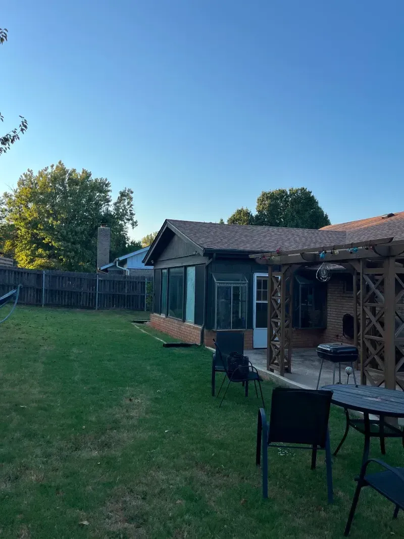 Lawn with outdoor seating, a building, and a screened-in structure with a clear blue sky above.