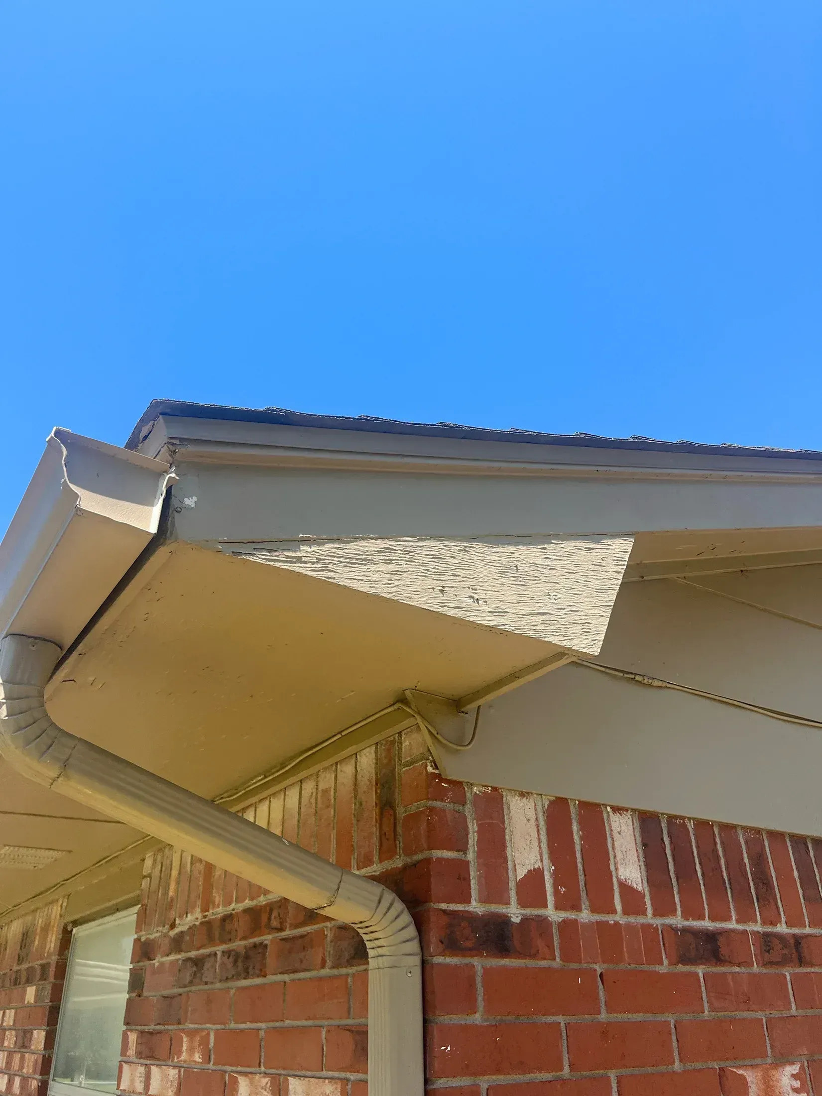 Brick building with tan soffit, gutter, and blue sky.