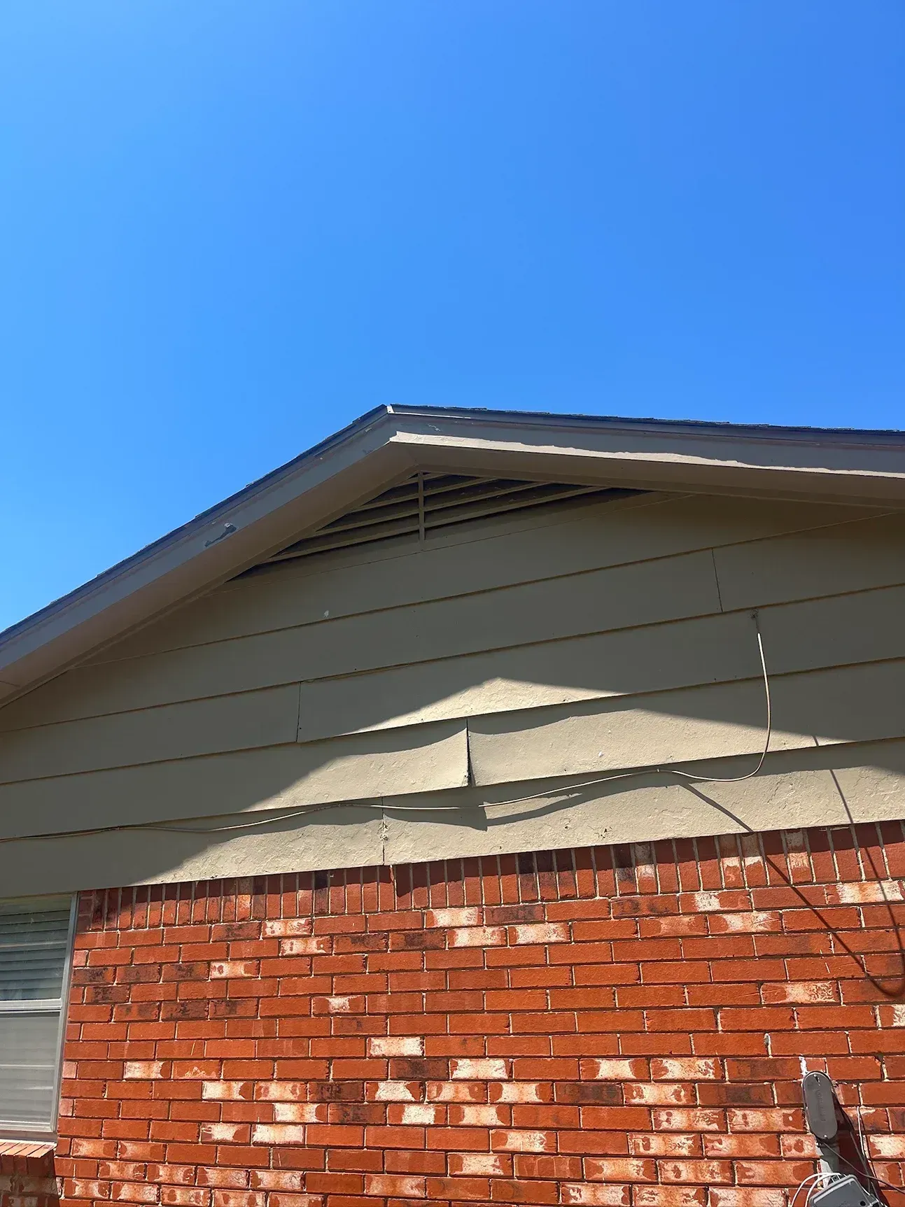 Red brick building with beige siding and blue sky, triangular roofline.