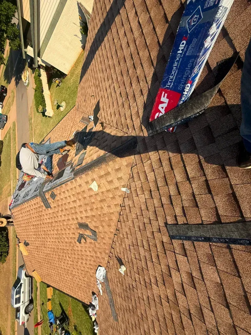 Roofers working on a brown shingle roof, repairing flashing at the ridge.
