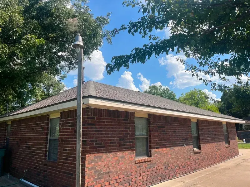 Red brick house with a dark roof and a silver pipe against a blue sky with fluffy clouds.