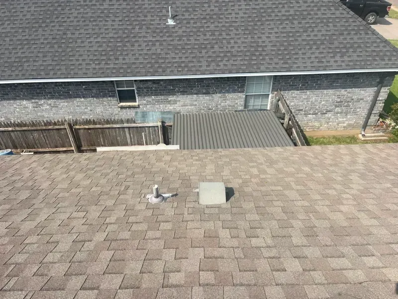 Roofs of two buildings with different colored shingles, a fence, and a glimpse of a vehicle.