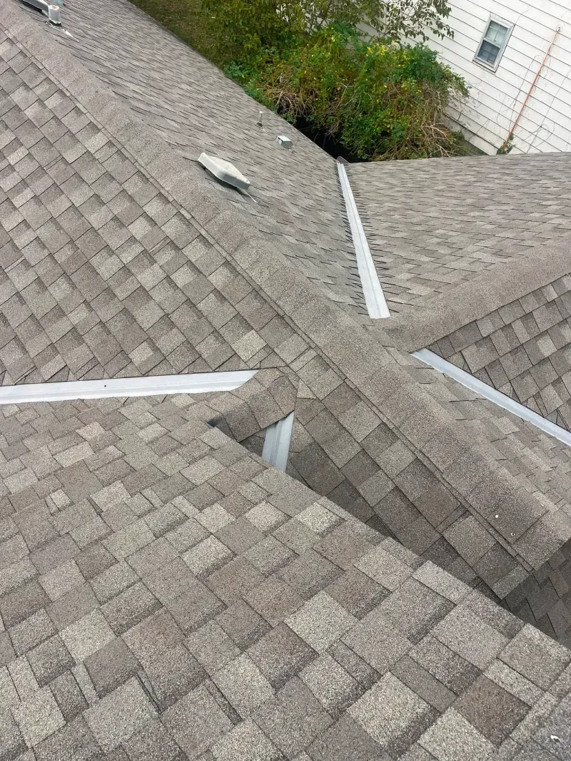 Asphalt shingle roof with flashing at a valley. Light brown shingles.