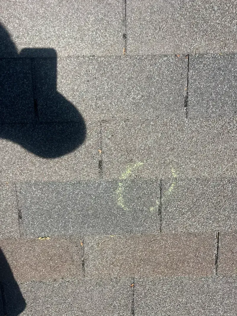 Close-up of gray asphalt shingles with chalk marks. Shadow of a person present.