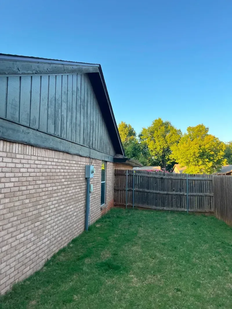 Brick house exterior with a grassy yard and wooden fence under a clear blue sky.