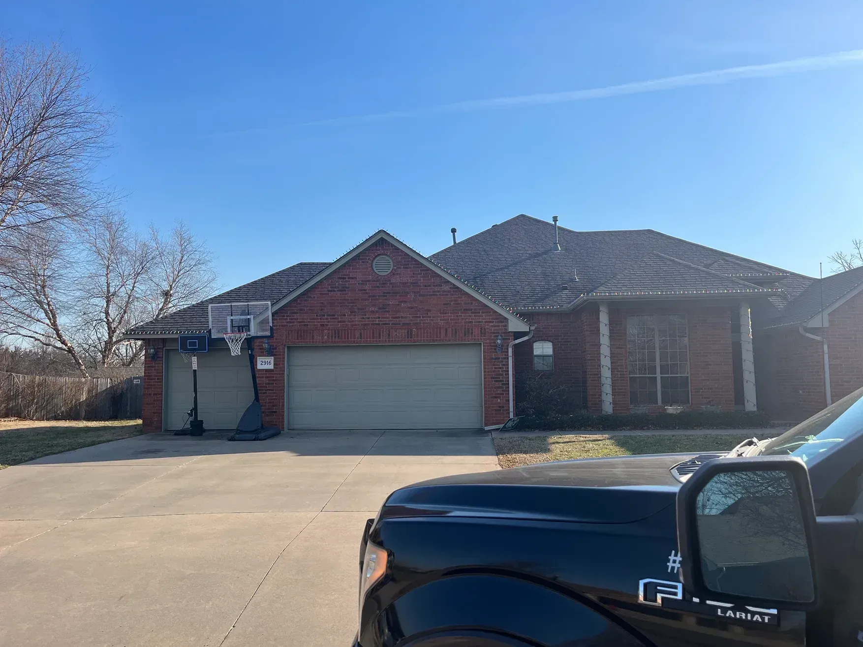 House with brick facade, two-car garage, basketball hoop, and a black pickup truck on a sunny day.