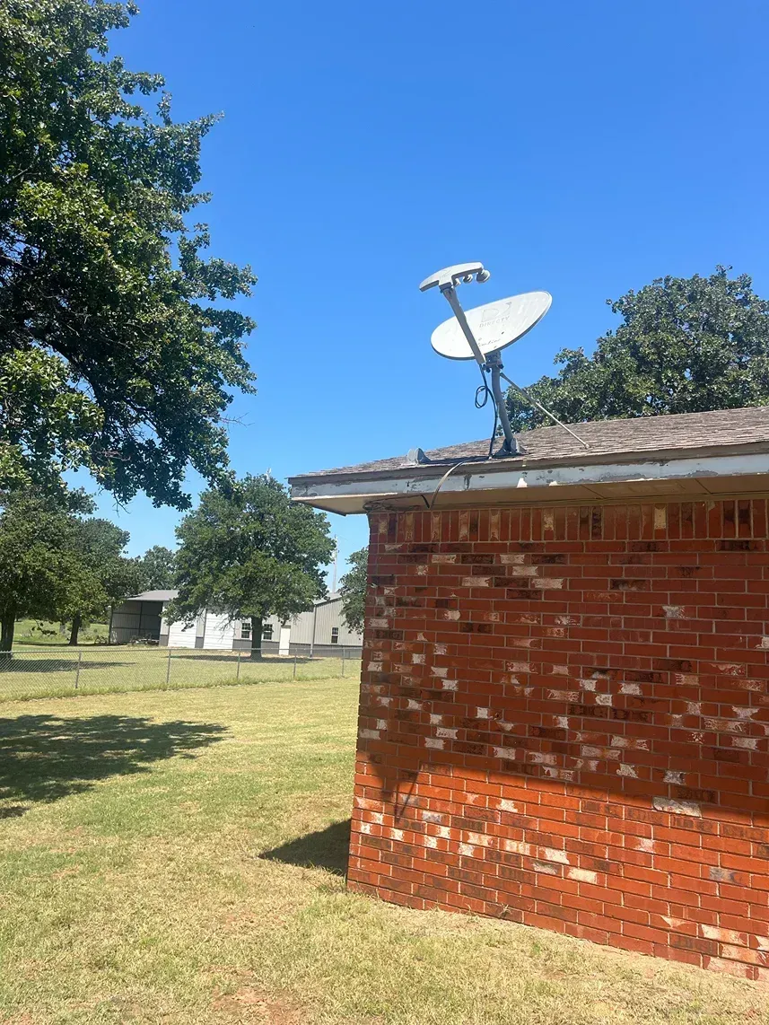 Satellite dish on a red brick building under a blue sky, trees in the background.