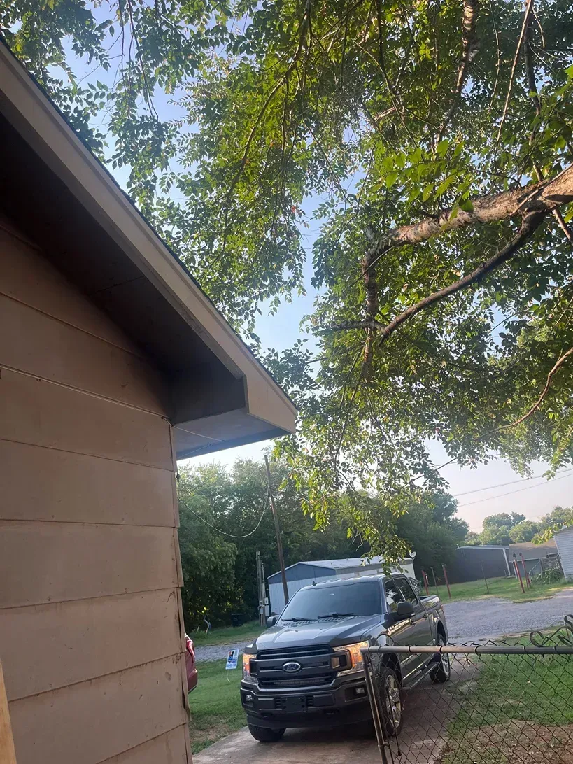 Brown house exterior with a pickup truck parked underneath tree branches.