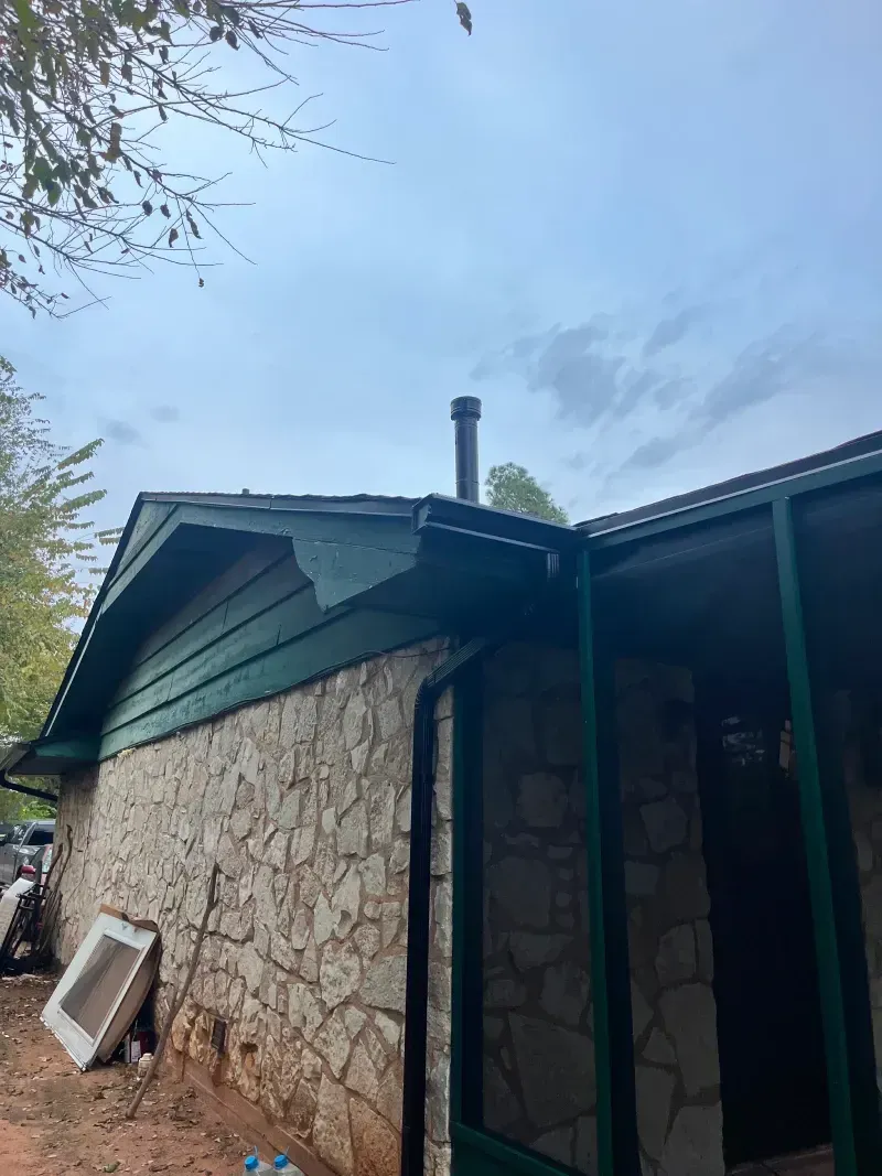 Stone building with green trim and a black chimney against a cloudy sky.