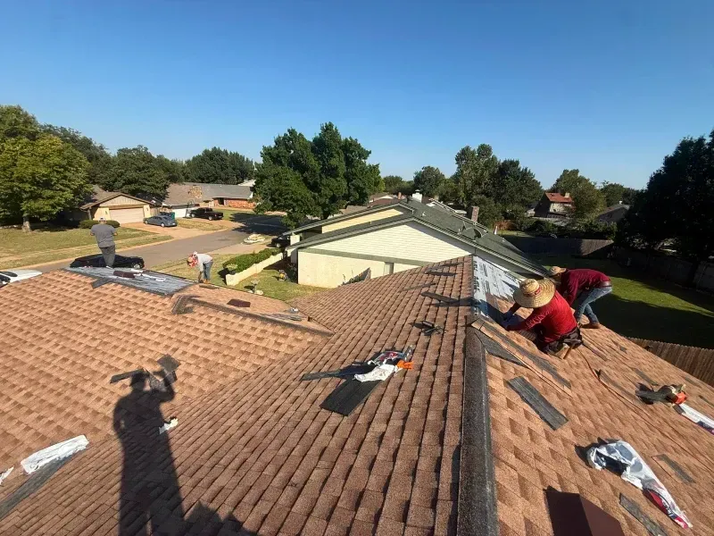 Roofers installing shingles on a house roof on a sunny day.