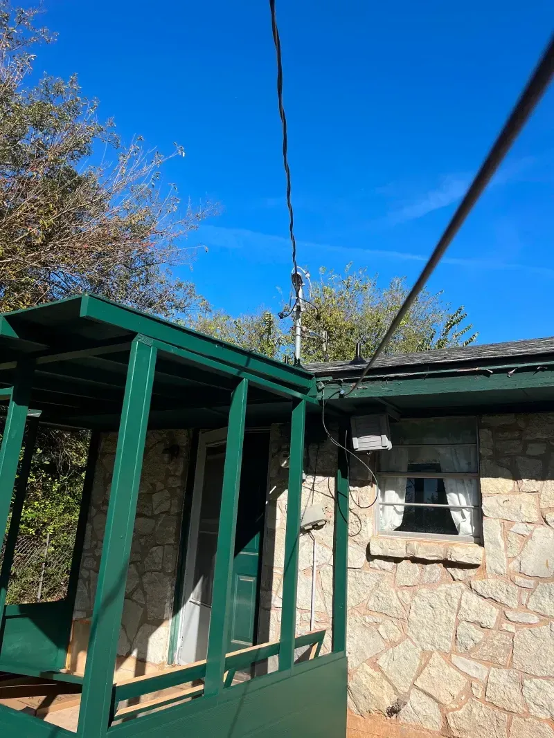 Green porch and stone building with power lines against a blue sky.