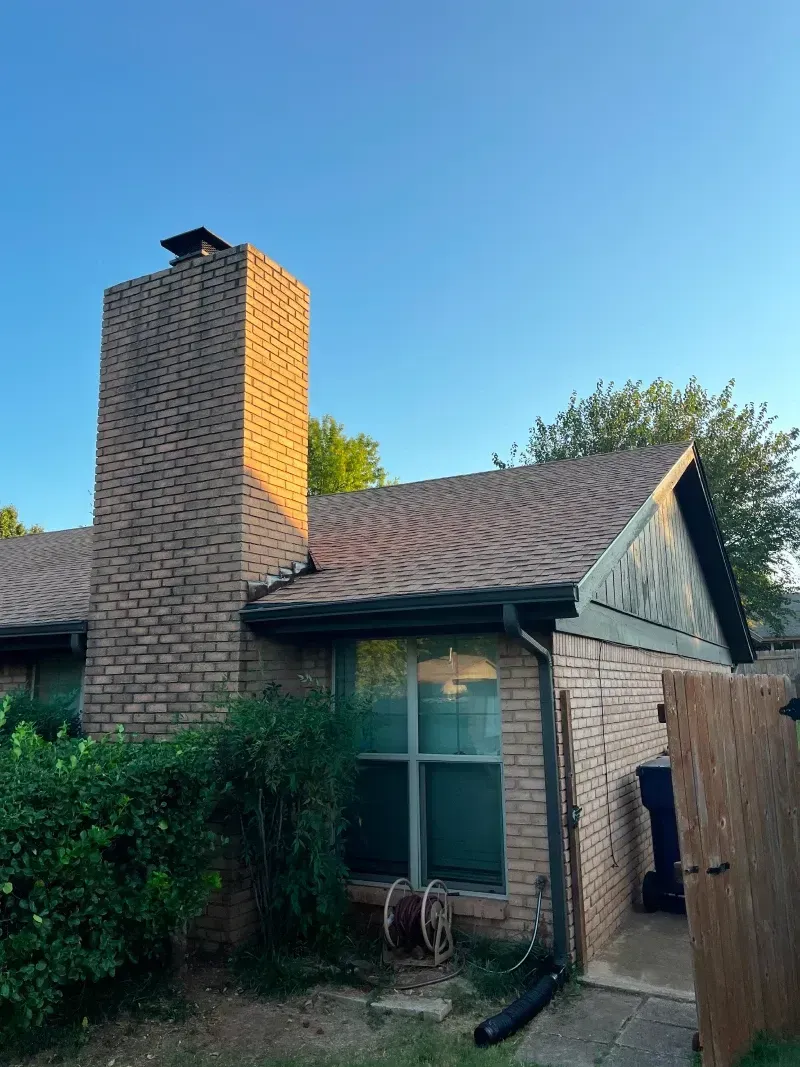 Brick chimney on a house with a brown roof; blue sky.