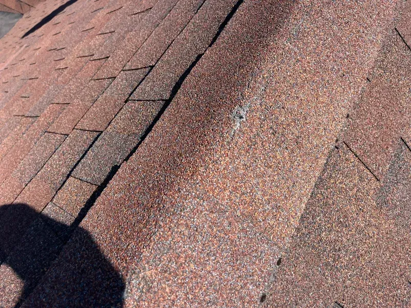 Close-up of a weathered asphalt shingle roof, showing a small area of damage and faded granules.