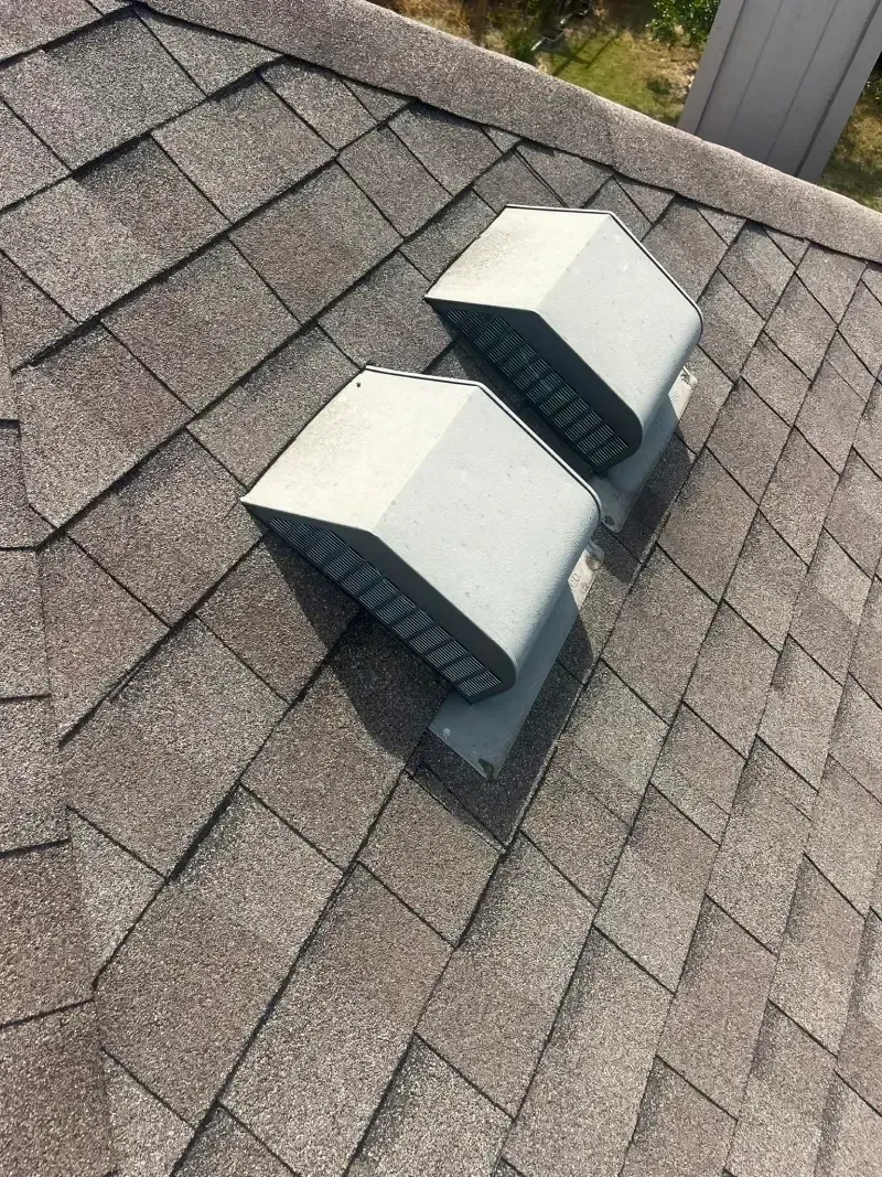 Two gray roof vents on a shingled roof.