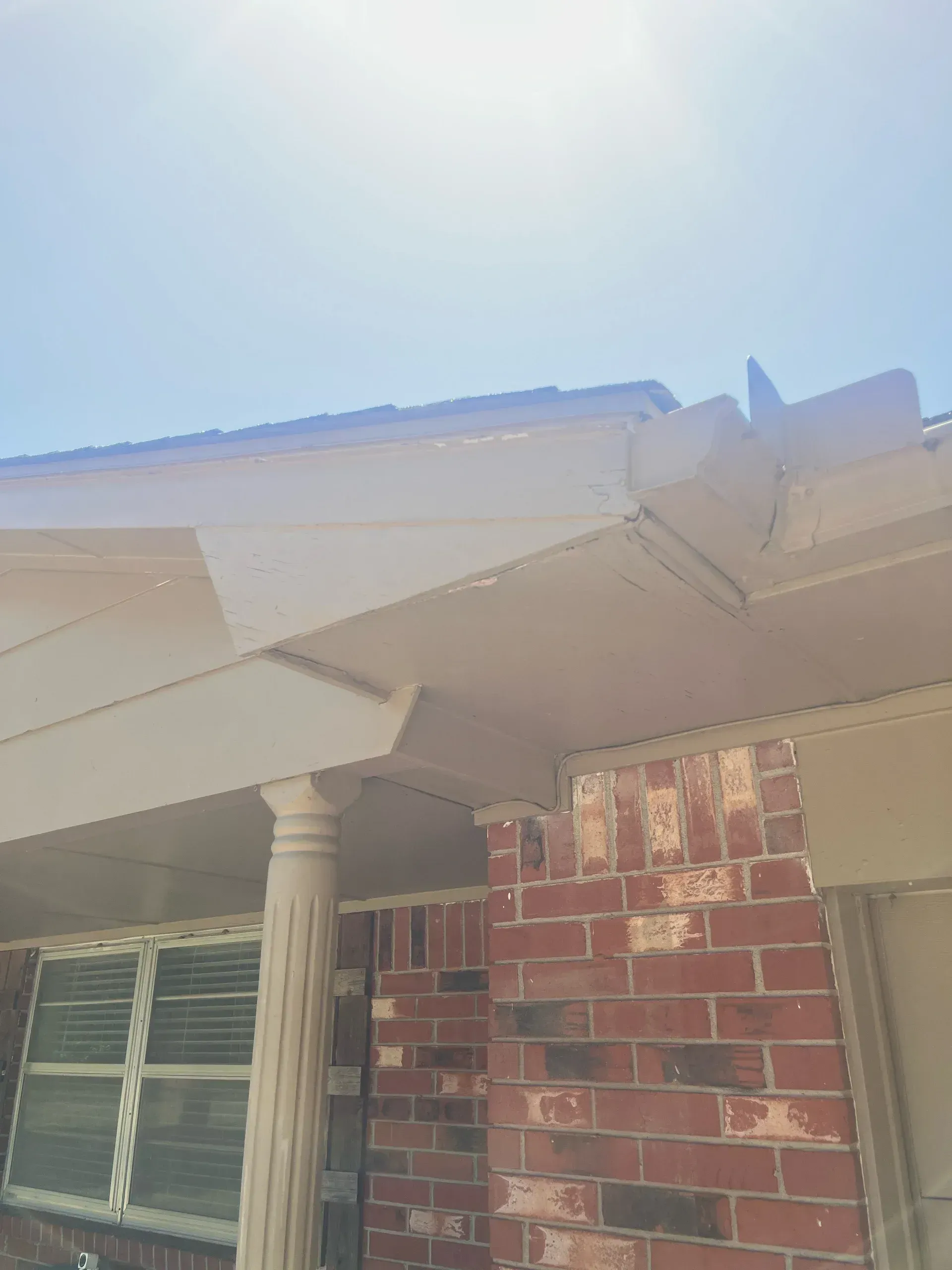 Brick house with white trim, column, and partial roof; sunny day.