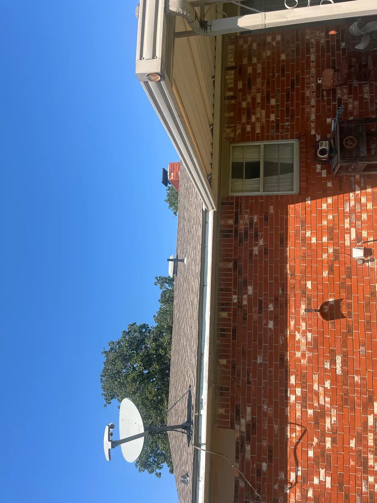 Brick building exterior with satellite dish, gutter, window, and blue sky.