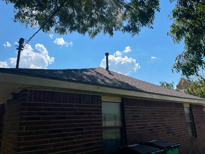Brick building with a dark roof and two metal pipes against a blue sky with fluffy white clouds.