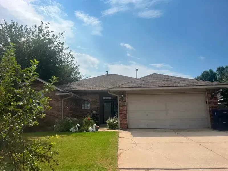 Single-story brick house with a brown roof and a two-car garage under a blue sky.