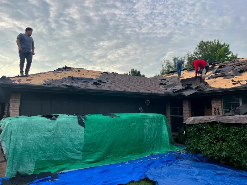 People on a damaged roof with a tarp covering the garage; overcast sky.