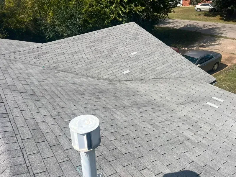 Gray shingled roof with a curved indentation and white ventilation pipe.