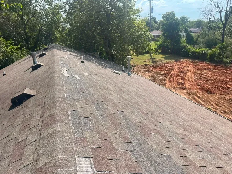 A shingled rooftop with weathered appearance, vents, and surrounding trees and yard.