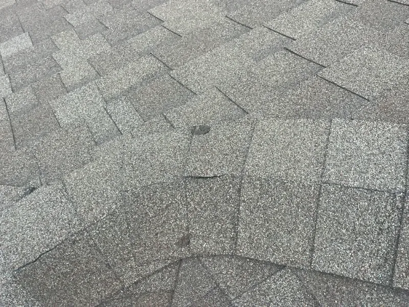Overhead view of weathered asphalt roof shingles. Gray and tan color with some damaged or missing sections.