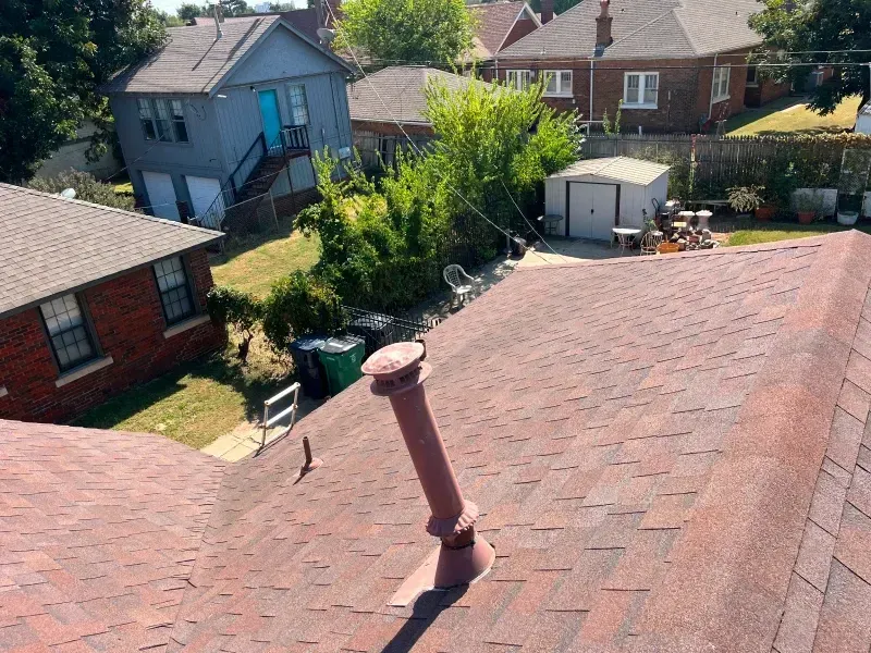 View of residential rooftops and backyards on a sunny day. Red brick, gray, and blue houses.