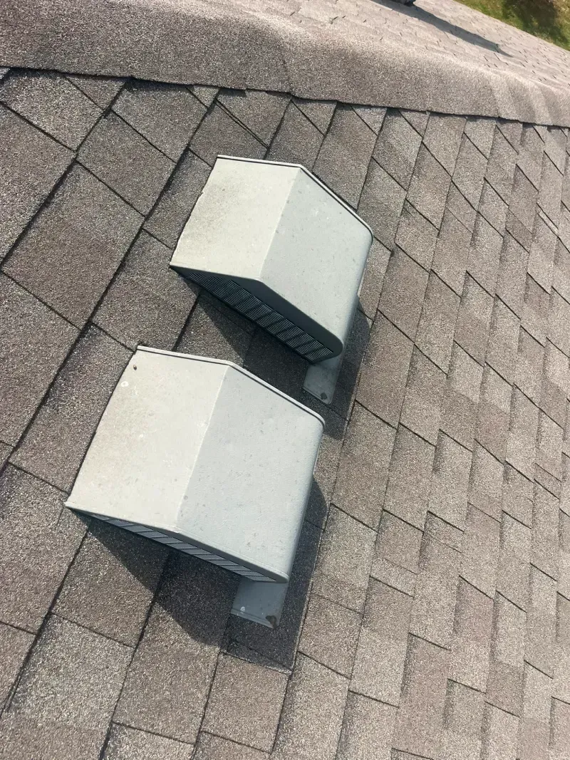 Two light-colored, box-shaped roof vents installed on a gray asphalt shingle roof.