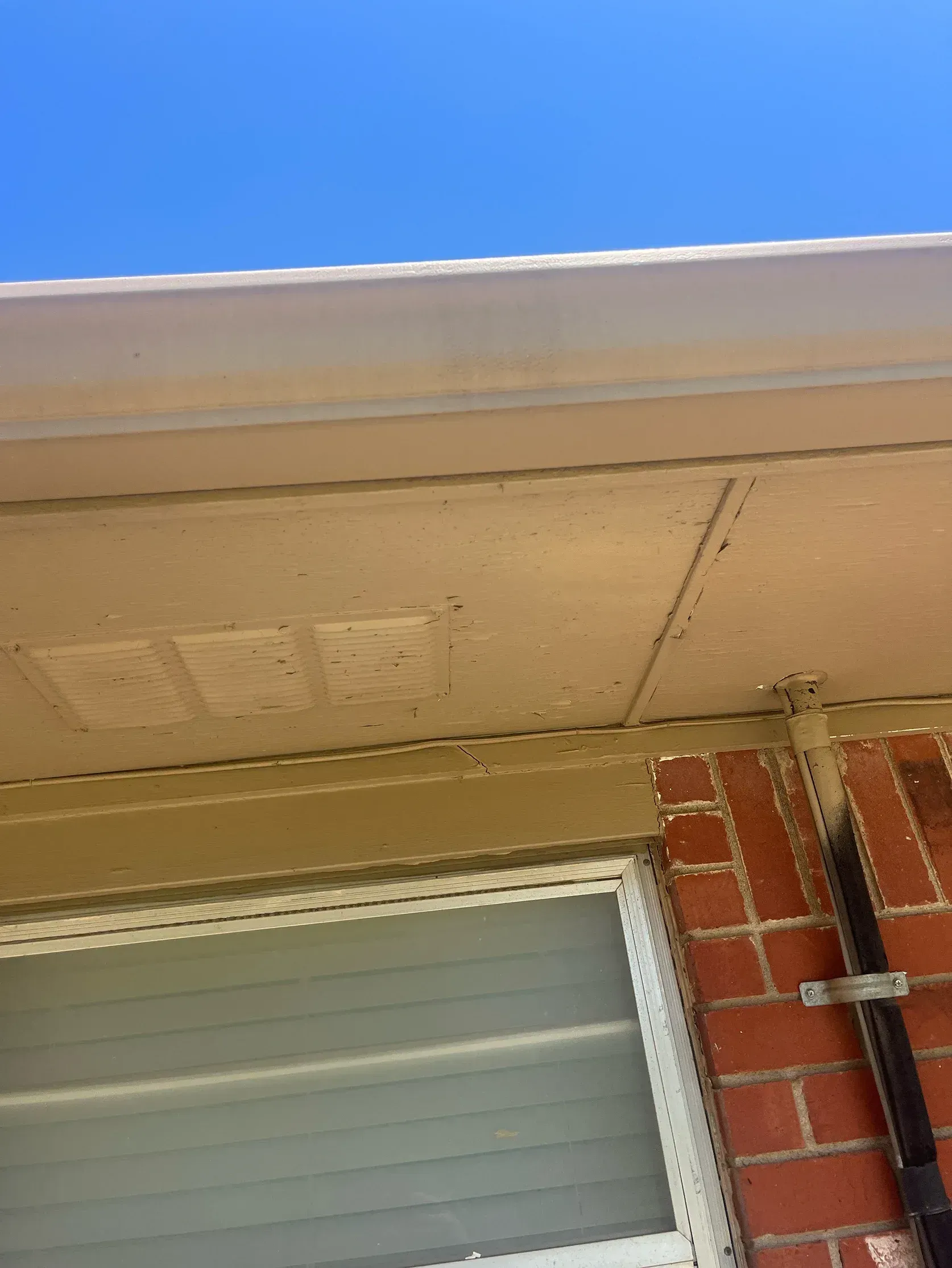 Exterior view of building's underside with a gutter, siding, and brick wall under a blue sky.