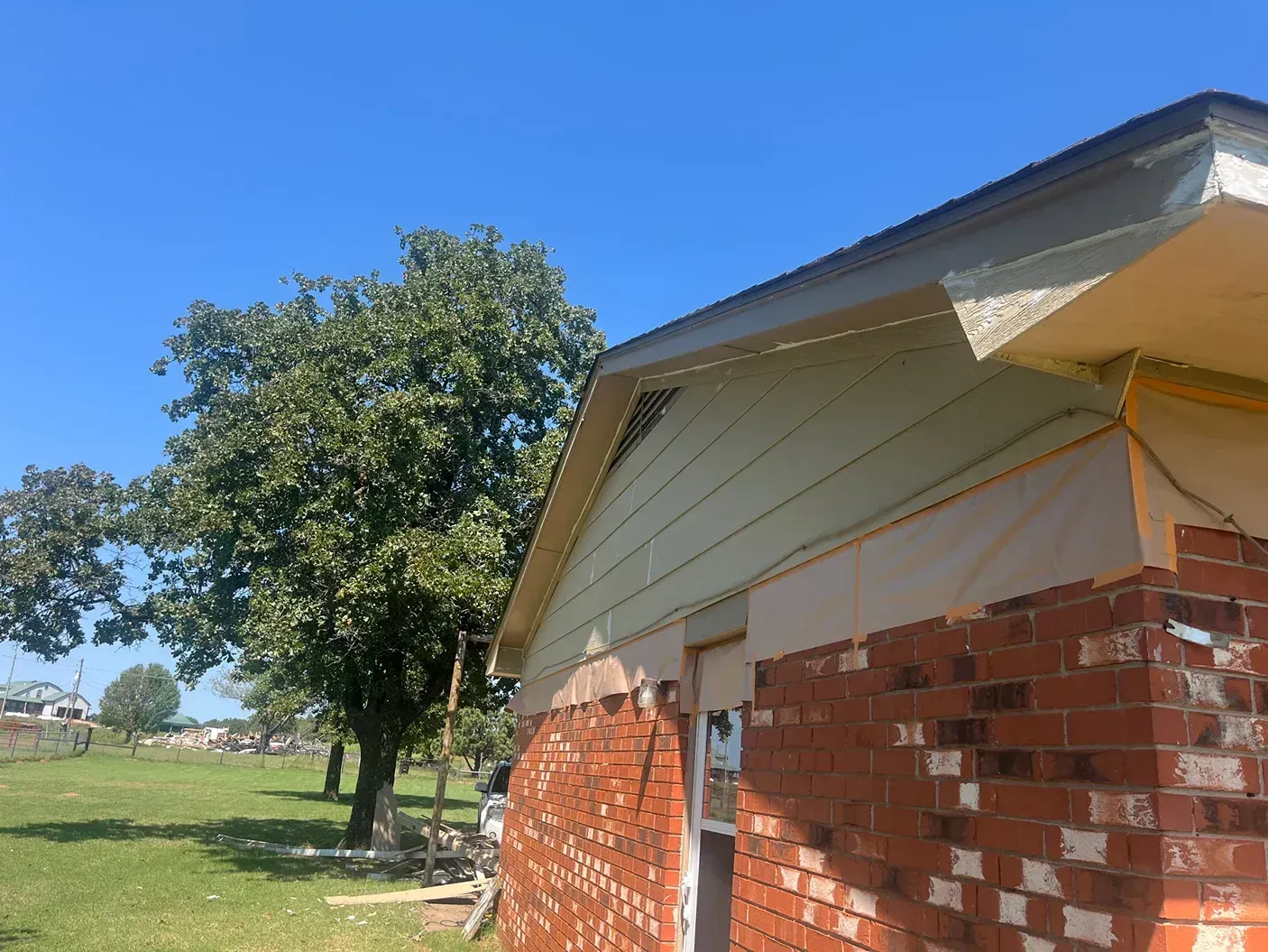 Brick building corner with green tree under a blue sky, siding partially removed.
