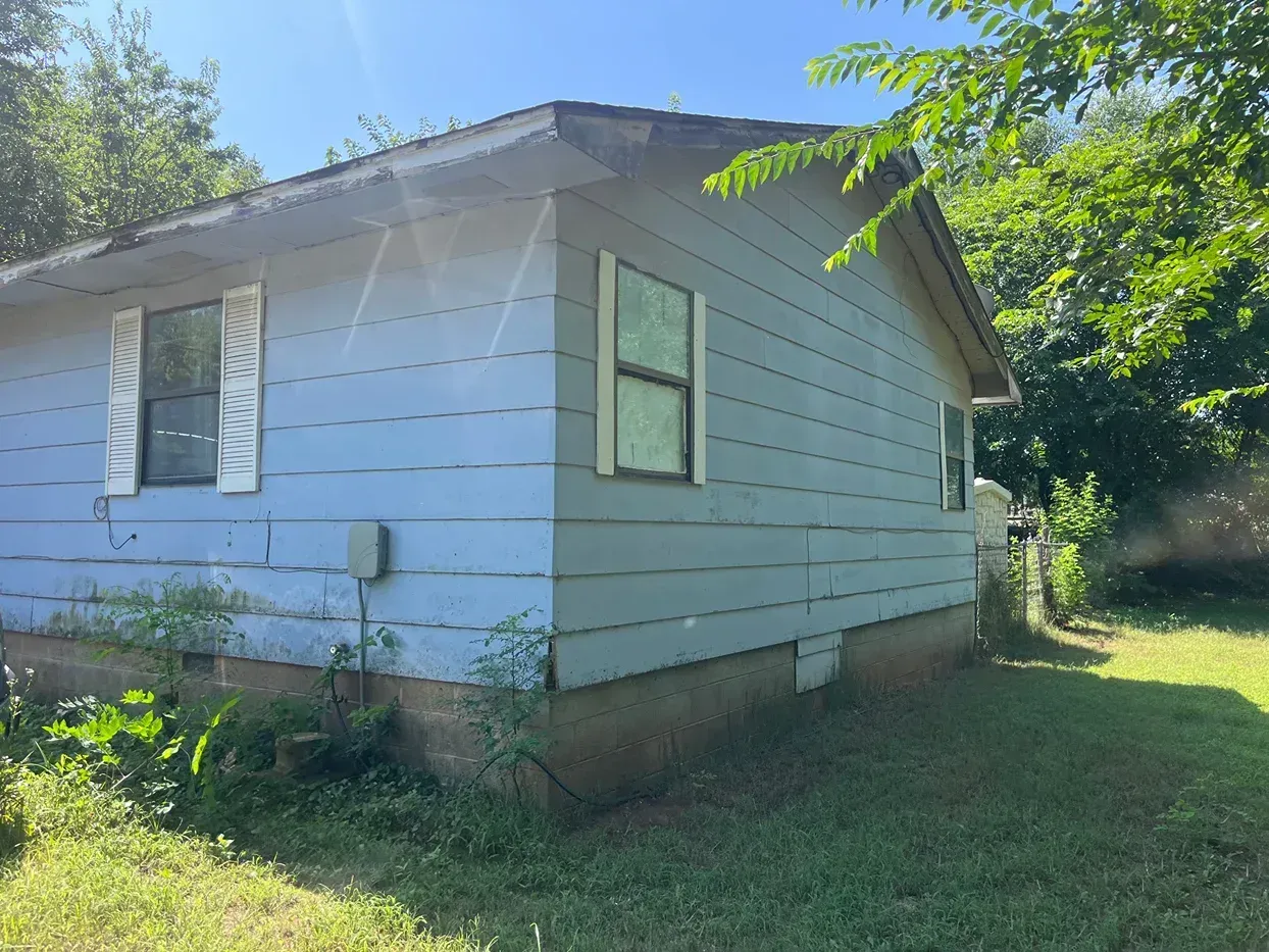 Side view of a blue-sided house with white window frames, set in a grassy yard, under a sunny sky.