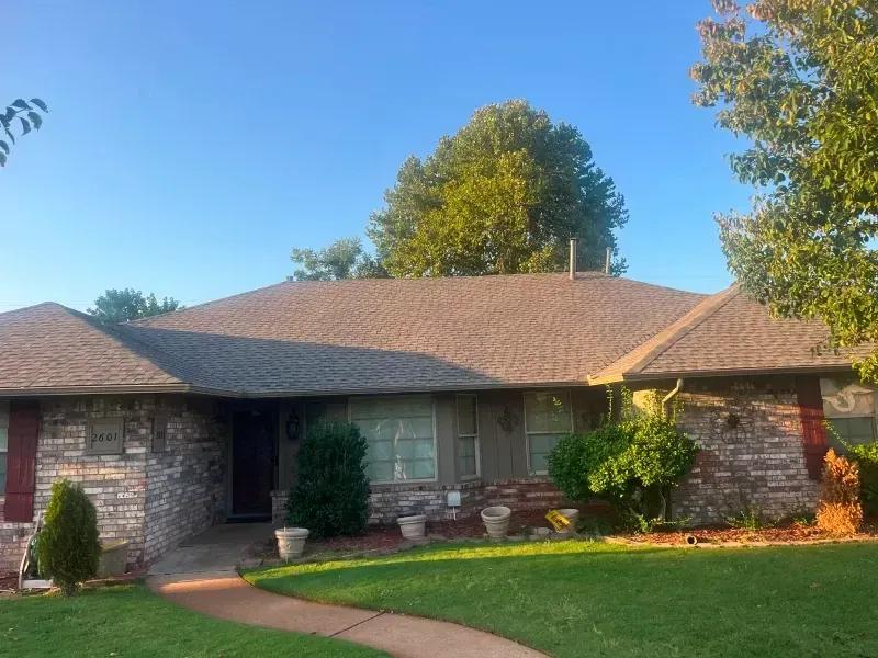 House with brick facade, brown roof, and green lawn under a blue sky.