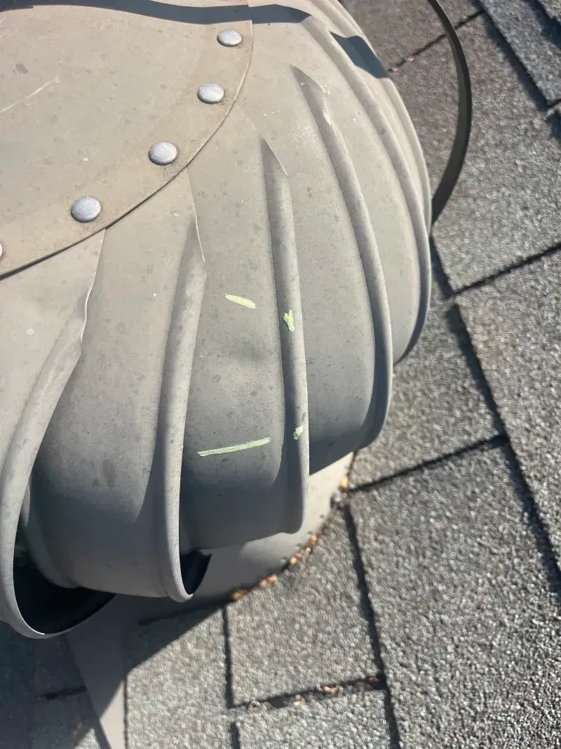 Roof vent on asphalt shingles. Gray metal turbine, close-up, outdoors on a sunny day.