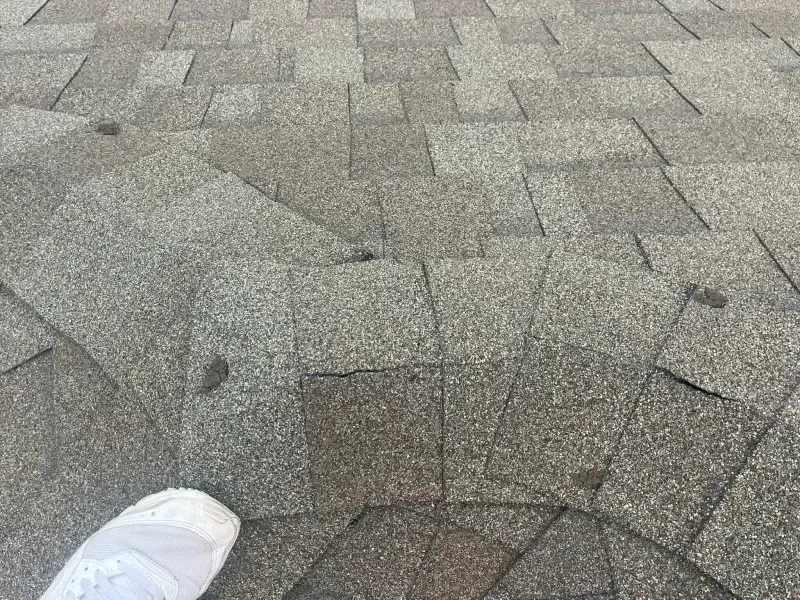 Overlapping gray asphalt roof shingles with a white shoe visible at the bottom left.