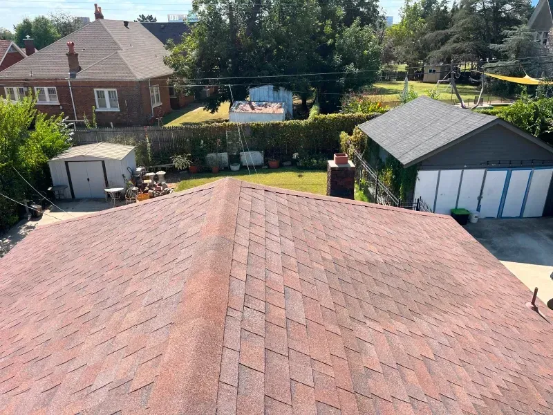 Red asphalt shingle roof, view of a backyard with shed and garage under a blue sky.