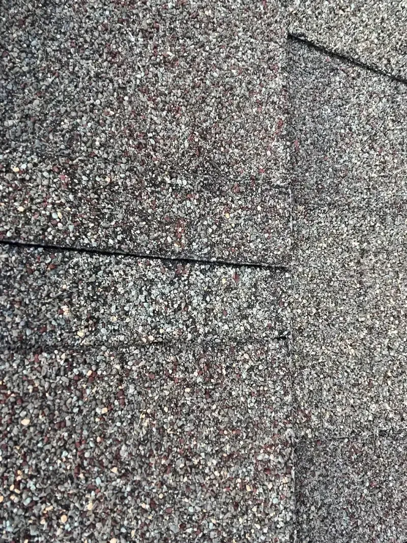 Close-up of asphalt shingle roof. Gray and brown granules with a horizontal crack.